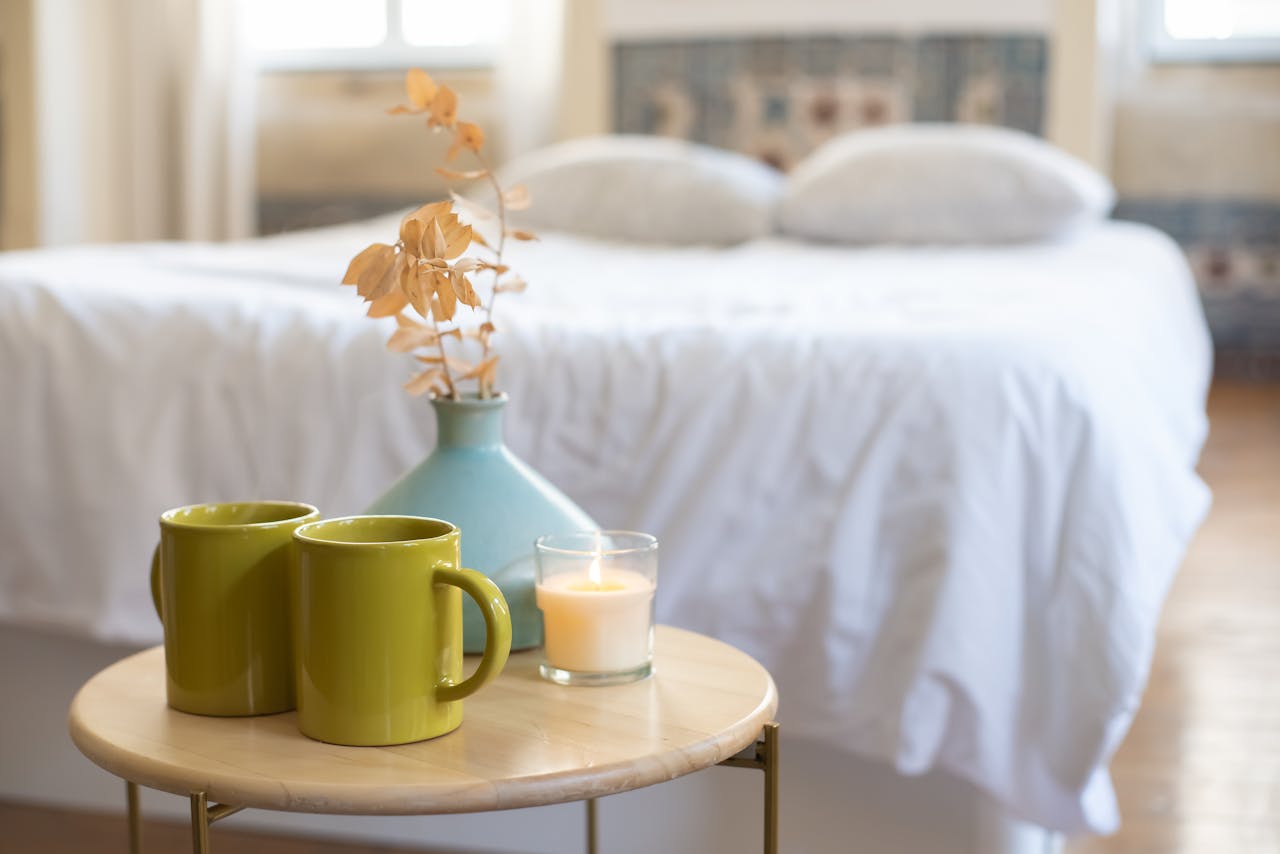 Inviting bedroom with a table setting featuring a candle, vase, and green mugs.