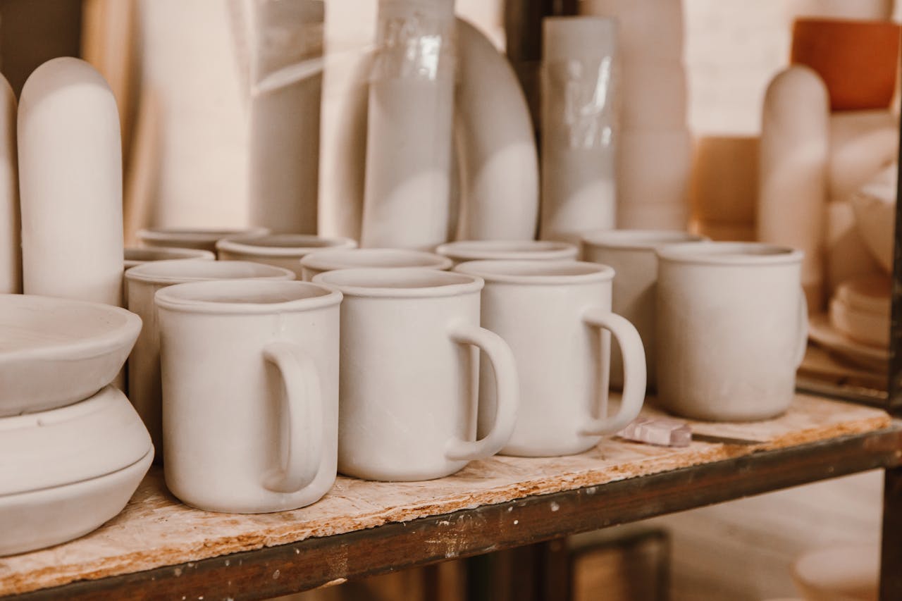 A collection of unfinished ceramic mugs arranged on a shelf awaiting glazing.